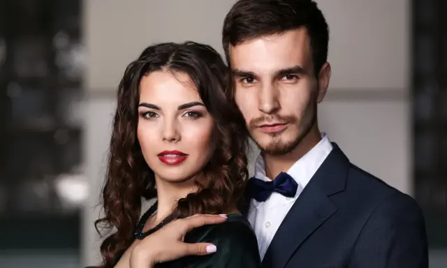 Elegancka para, niczym koziorożec i baran, pozuje do zdjęcia. Ona w ciemnej sukni, on w granatowym garniturze.