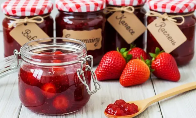 Bocaux de confiture de fraise faits maison, avec des fraises fraîches et une cuillère remplie de confiture.