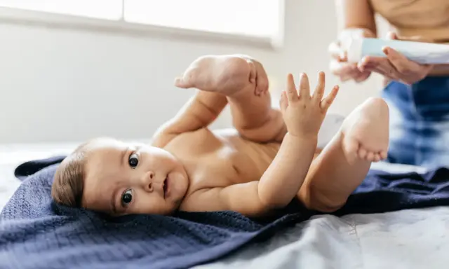 Uroczy noworodek leży na granatowym kocyku, podnosząc nóżki. Mama przygotowuje się do masażu brzuszka, by ulżyć mu w **gazach u noworodka**.