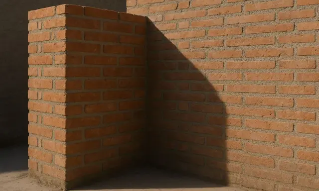 Esquina de un muro medianero entre vecinos, construido con ladrillos de color terracota y cemento gris. Una sombra diagonal cruza la pared.