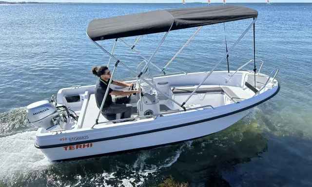 Ce bateau Terhi 450, propulsé par un moteur Honda de 6 cv, navigue sur une mer calme. Idéal pour explorer les côtes.