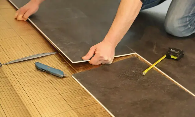 Pose de dalles de sol sur une sous-couche isolante. Un cutter et un mètre sont à portée de main pour comment isoler un sol efficacement.