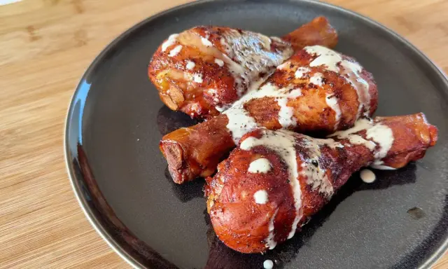 Tre succulenti fusi di pollo arrostiti, conditi con spezie e nappati con una cremosa salsa bianca, serviti su un piatto scuro.