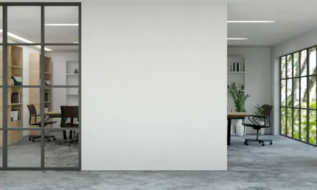 Un moderno tabique de cristal separa una sala de reuniones con estanterías de madera de una oficina con vistas a un jardín frondoso.