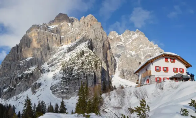 Rifugio alpino innevato ai piedi di maestose vette rocciose, un vero spettacolo di posti belli in montagna Veneto inverno.