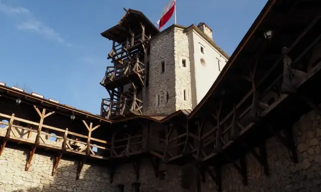 Zamek w Korzkwi z drewnianymi gankami i wieżą, na której powiewa polska flaga.