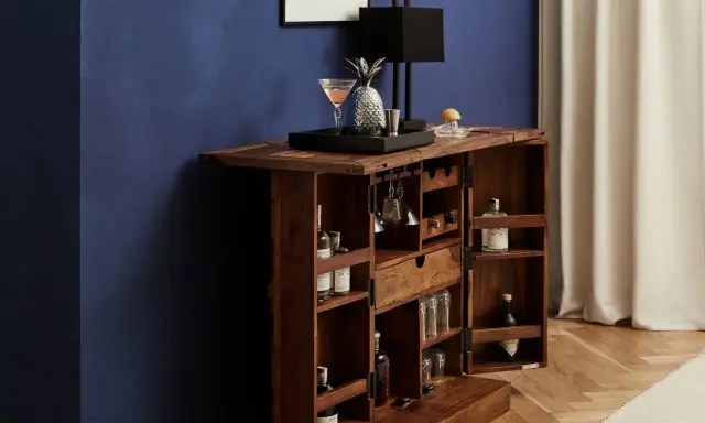 Elegante mobile bar design in legno scuro, aperto, con bottiglie, bicchieri, lampada e decorazioni.