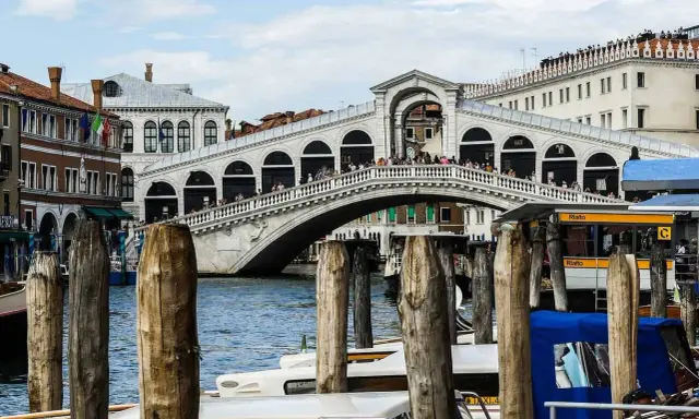 Le célèbre pont du Rialto à Venise, animé par des touristes, surplombe le Grand Canal où naviguent des gondoles et des taxis nautiques.
