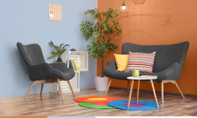 Nowoczesny salon z szarymi fotelami i kanapą, akcentem jest ściana w kolorze oranżowym.