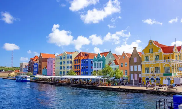 Färgstarka hus längs en kaj, en båt i vattnet. Här kan man se var ligger Curacao, en karibisk pärla.