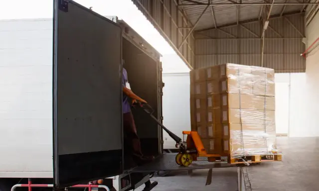 Un operario usa una carretilla para el transporte de materiales, cargando cajas en un camión.
