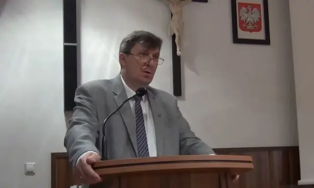 Mężczyzna w garniturze przemawia, za nim krzyż i godło Polski. Może mówi o cnotach kardynalnych.
