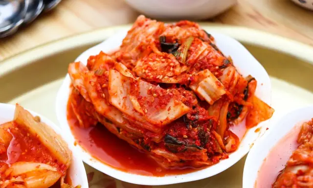 Kilka białych miseczek z pikantnym, czerwonym kimchi na drewnianym tle.