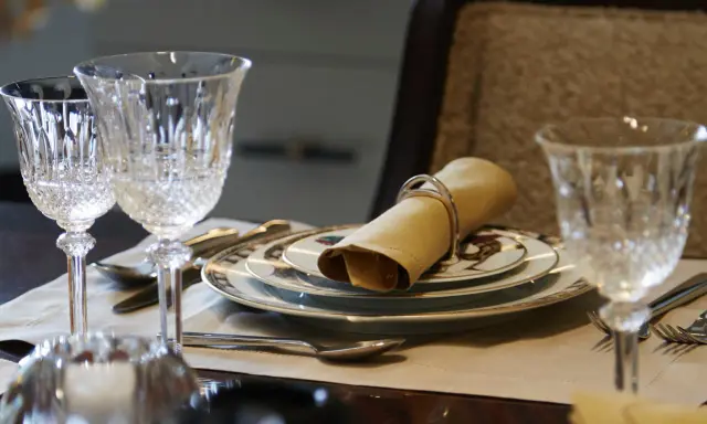 Verre à pied taillé, assiettes décorées, serviette en tissu joliment pliée : une table dressée pour le service à la française.