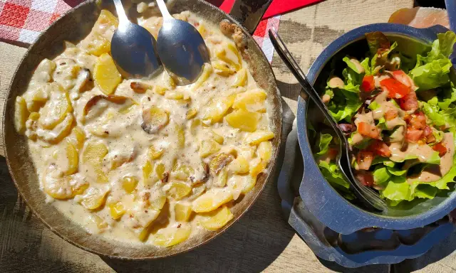 Plat de pommes de terre crémeuses, une spécialité auvergnate, servi dans une poêle avec une salade fraîche.