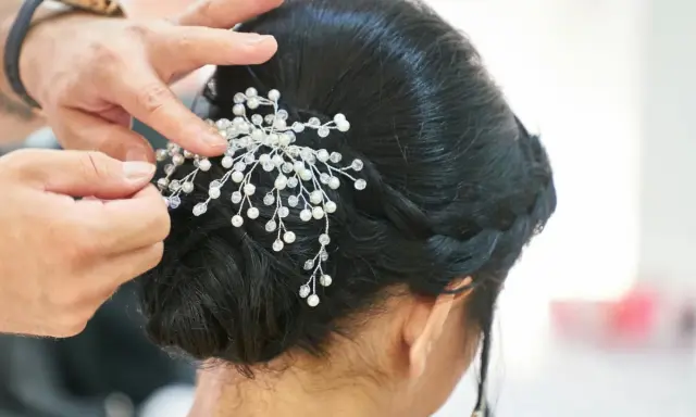 Manos expertas ajustan un tocado de perlas y cristales a un juvenil recogido de boda, creando un look elegante y romántico.