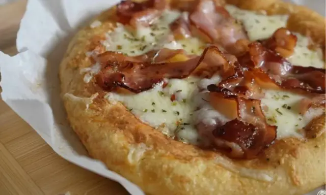 Pyszna pizza z mozzarellą i chrupiącym boczkiem, posypana ziołami. Idealna na szybki lunch.