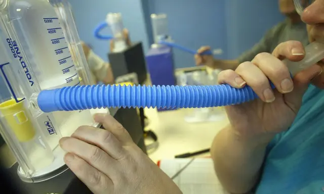 Person nutzt ein Spirometer für einen Lungenfunktionstest. Der Asthmaspray ist nicht sichtbar, aber das Gerät hilft bei der Diagnose.