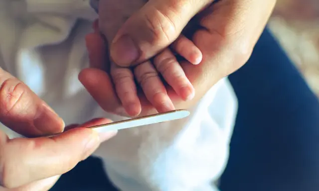 Mani adulte limano delicatamente le unghie di un neonato, un momento di cura che mostra quando si possono tagliare le unghie ai neonati.