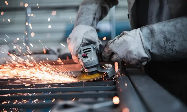 Pracownik w rękawicach szlifuje metal, sypią się iskry. Wypadek przy pracy? Protokół powypadkowy wymaga dokumentacji.