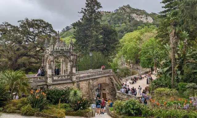 Ein märchenhafter Sintra Garten mit einer steinernen Brücke, üppiger Vegetation und Besuchern, die die Aussicht genießen.