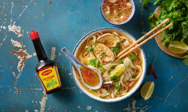 Aromatyczna zupa pho z kurczakiem, makaronem ryżowym, limonką i świeżą kolendrą. Obok butelka przyprawy Maggi.