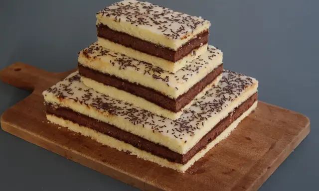 Trois parts de napolitain sans gluten empilées sur une planche en bois, garnies de vermicelles au chocolat.