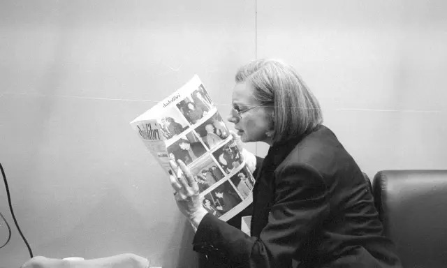 Fleur Jaeggy, con occhiali e giacca scura, legge un giornale con foto.