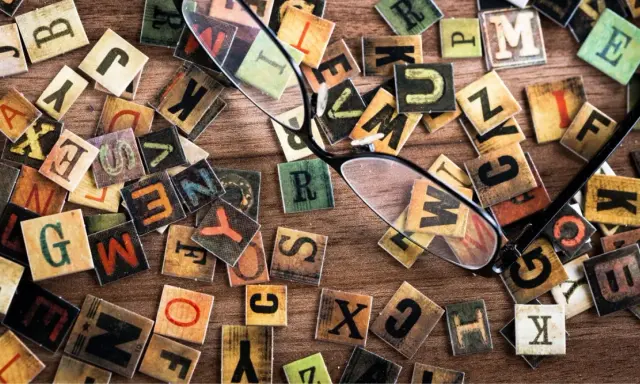 Un occhio attento scruta le lettere sparse, una figura retorica che unisce due termini contraddittori, creando un caos ordinato di parole.