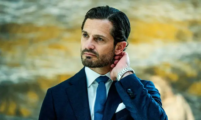 Prins Carl Philip i mörkblå kostym, vit skjorta och blå slips. Hans hand vilar bakom örat, en detalj som speglar hans intresse för carl philip design.