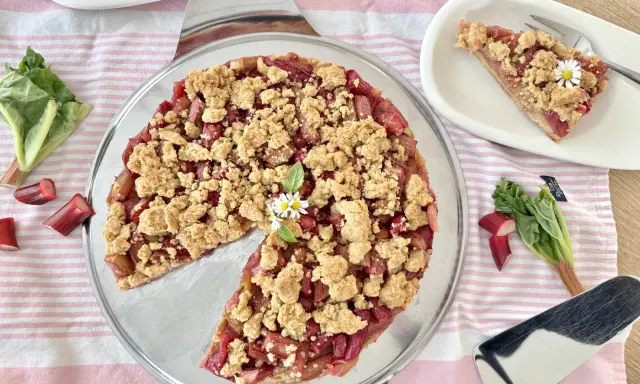 Ein köstlicher Rhabarber Streuselkuchen mit frischem Rhabarber und knusprigen Streuseln, garniert mit kleinen Gänseblümchen.