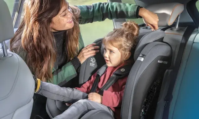 Mama poprawia zagłówek w foteliku samochodowym 9-36 dla swojej córki.