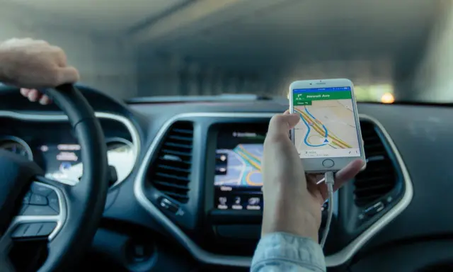 Mano al volante, móvil con mapa GPS mostrando cómo funciona un localizador GPS para coche.