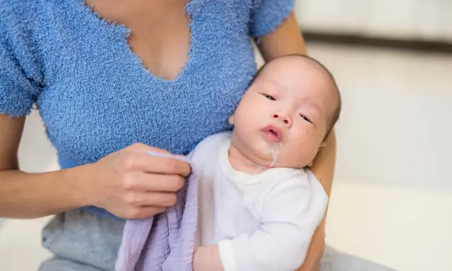 Un neonato con rigurgito, tenuto in braccio dalla madre che ha un panno viola.