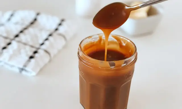 Une cuillère verse un caramel beurre salé liquide dans un pot en verre. Parfait pour une recette gourmande.