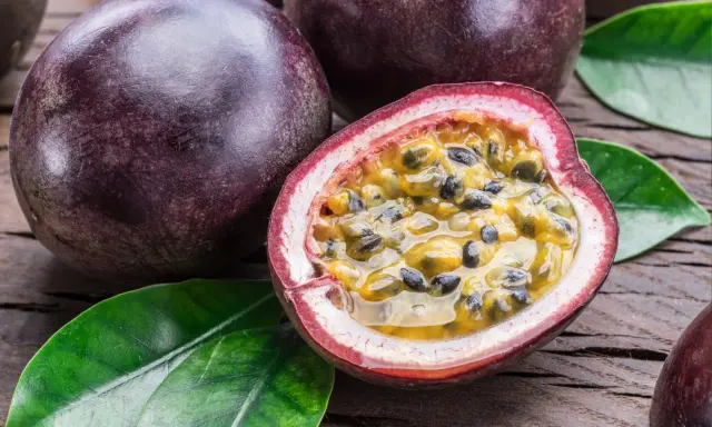 Dunkle, runde Früchte liegen auf Holz. Eine davon ist aufgeschnitten und zeigt das saftige Fruchtfleisch mit Kernen – eine köstliche Passionsfrucht Maracuja.