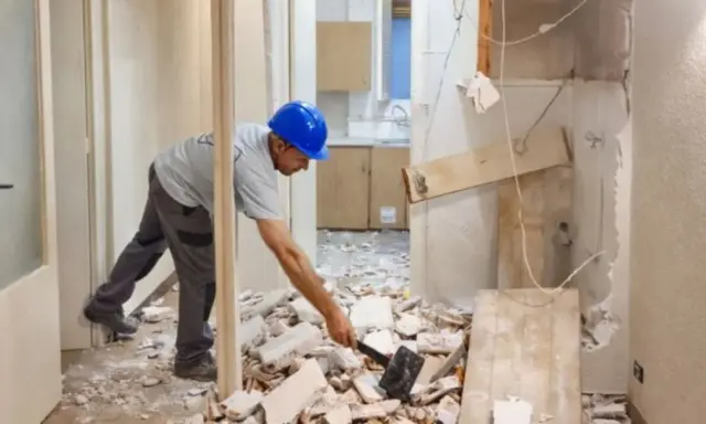 Hombre con casco azul rompiendo escombros con un mazo. Parece que él mismo **puedo tirar un tabique** para renovar la cocina.