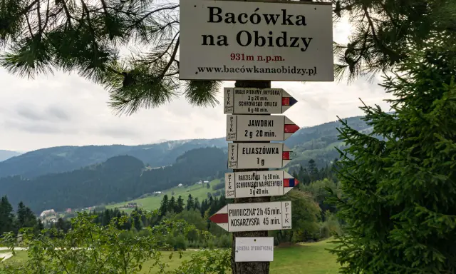 Tablica z drogowskazami na szlak na Radziejową. W tle górzysty krajobraz Beskidu Sądeckiego.