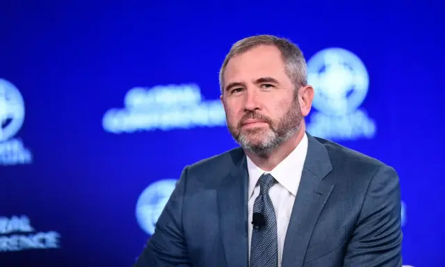 Brad Garlinghouse, CEO Ripple, w niebieskim garniturze, z brodą, na tle niebieskiej sceny z logo Global Conference.