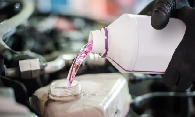 Mano con guante negro vierte líquido rosa, agua de motor coche, en depósito.