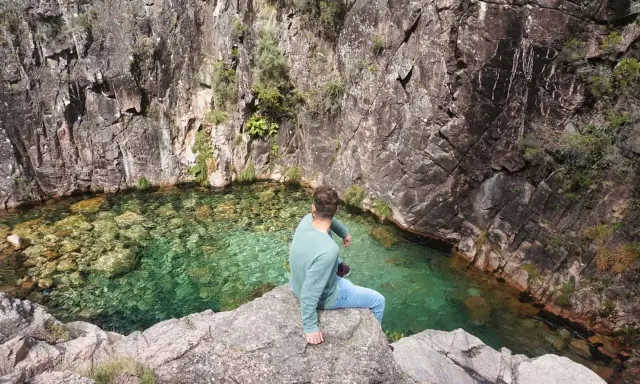 Mann sitzt auf Felsen am kristallklaren Wasser des Peneda-Gerês-Nationalparks.
