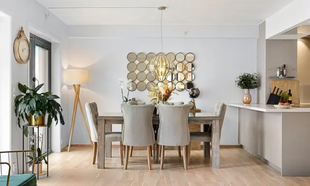 Comedor elegante con mesa de madera y sillas tapizadas, sobre un suelo sisal. Decoración con espejos circulares y lámpara colgante.