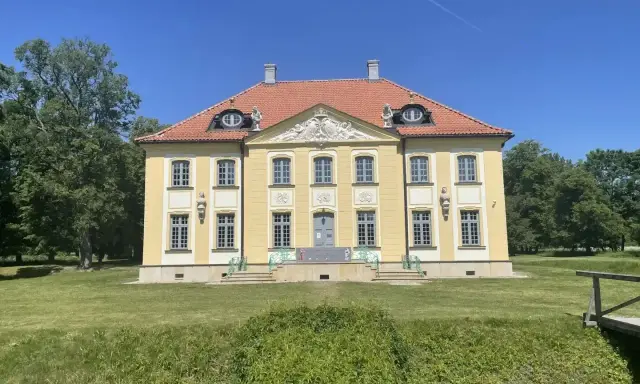Piękny, żółty pałac w Choroszczy z czerwonym dachem, otoczony zielenią i błękitnym niebem.