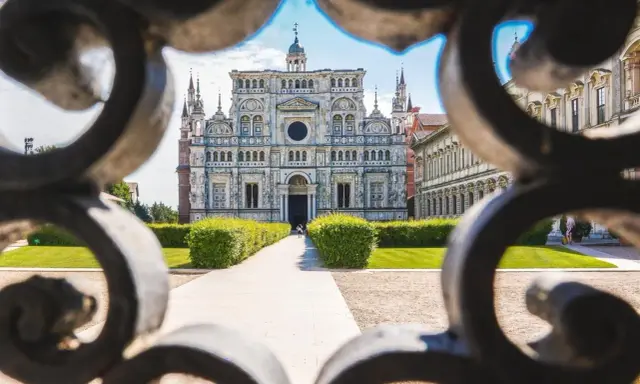 La Certosa di Pavia, un capolavoro rinascimentale, vista attraverso un cancello decorato. Un percorso conduce alla maestosa facciata.