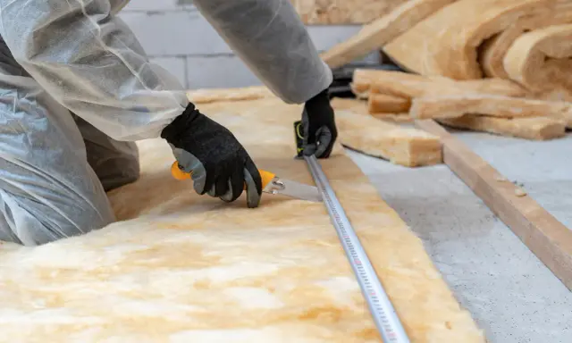 Un ouvrier mesure et coupe un isolant hydrophile pour une isolation thermique optimale.