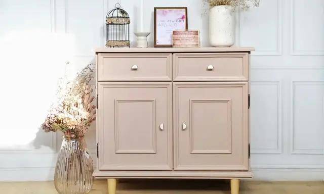 Meuble en bois peint en rose poudré, avec deux tiroirs et deux portes. Décoration florale et cage ornementale sur le dessus.