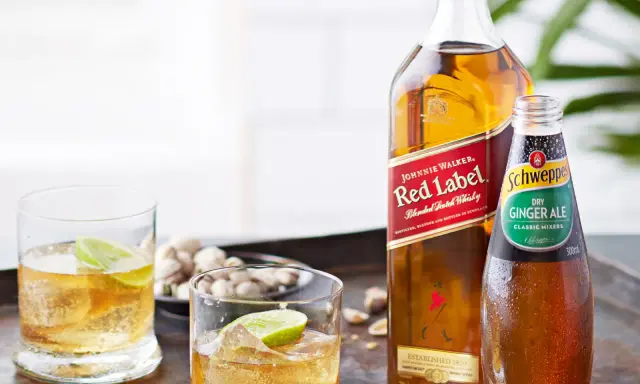 Butelka Johnnie Walker Red Label, butelka Schweppes Ginger Ale i dwa drinki z lodem i limonką.