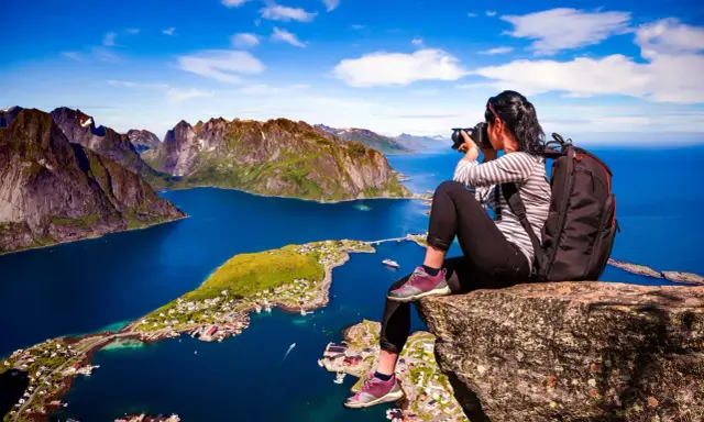 En fotograf fångar de dramatiska vyerna över Lofoten sevärdheter, med branta berg och en idyllisk by vid det blå havet.