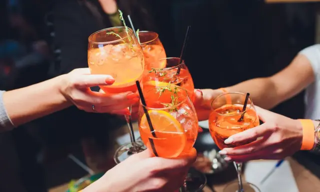 Hände stoßen mit Aperol Spritz an. So einfach wie man ihn macht, so erfrischend ist er!