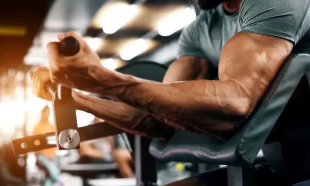 Ein Mann trainiert seinen Bizeps-Muskel an einem Gerät im Fitnessstudio. Die Adern treten deutlich hervor.